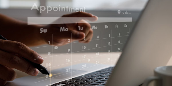 A person typing on their computer and a calendar is on the screen