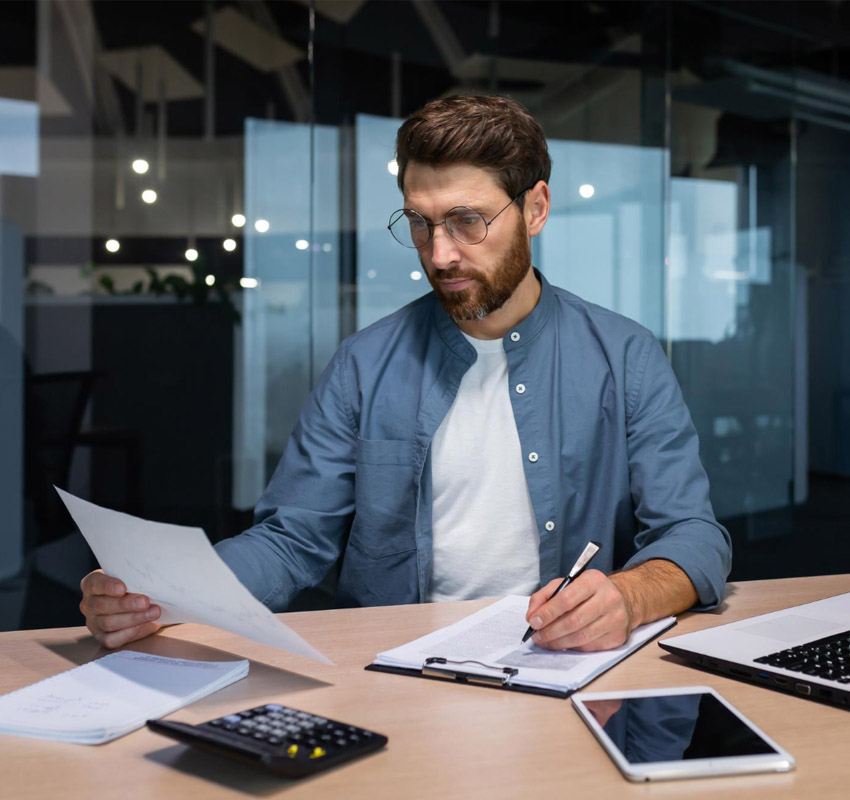 A man at his desk in an office writing notes and looking at a document