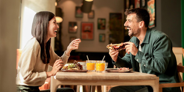 A man and women eating pizza and laughing at a restaurant