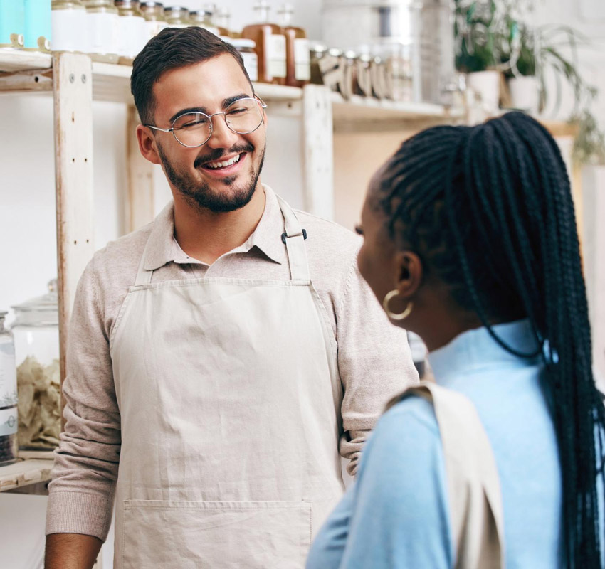 Man working in coffee shop smiling and talking to customer