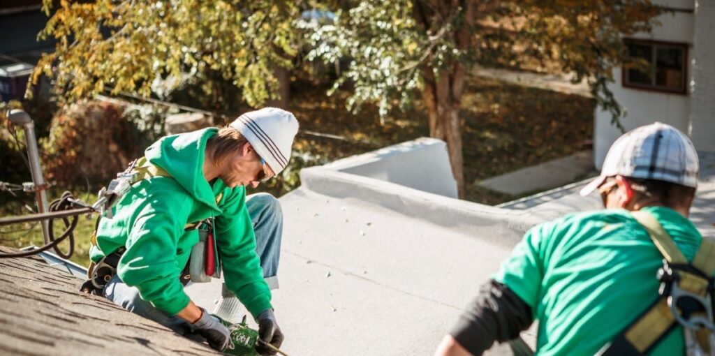Two people putting shingles on a roof